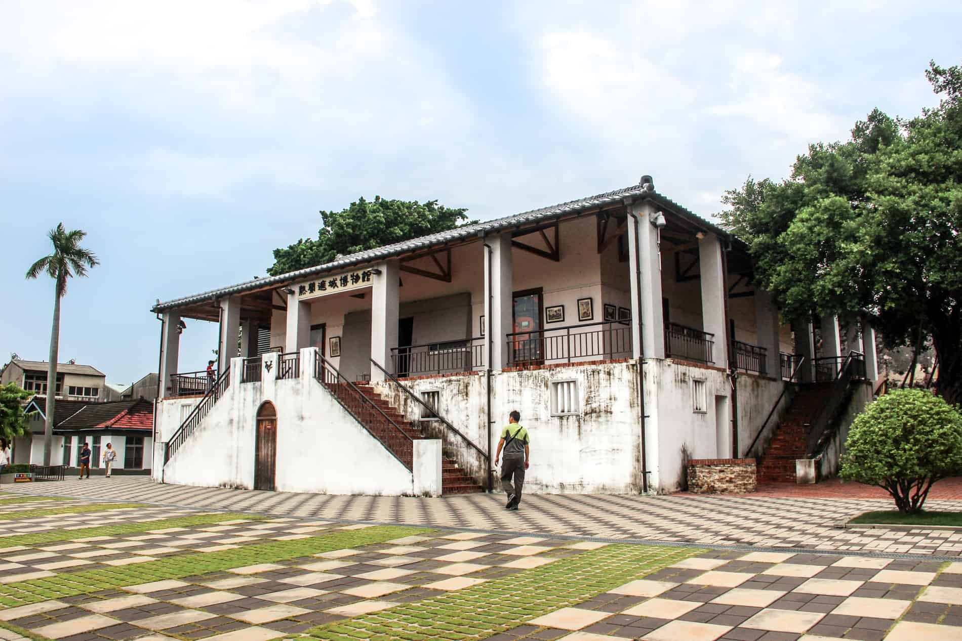 A man walks on chequered paving stones towards a white colonial-style building at Fort Zeelandia, Tainan. 